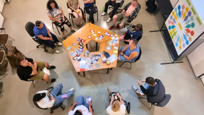 Profesionālās piemērotības noteikšanas nodarbībā ap galdu sasēdušies cilvēki un veic radošās aktivitātes